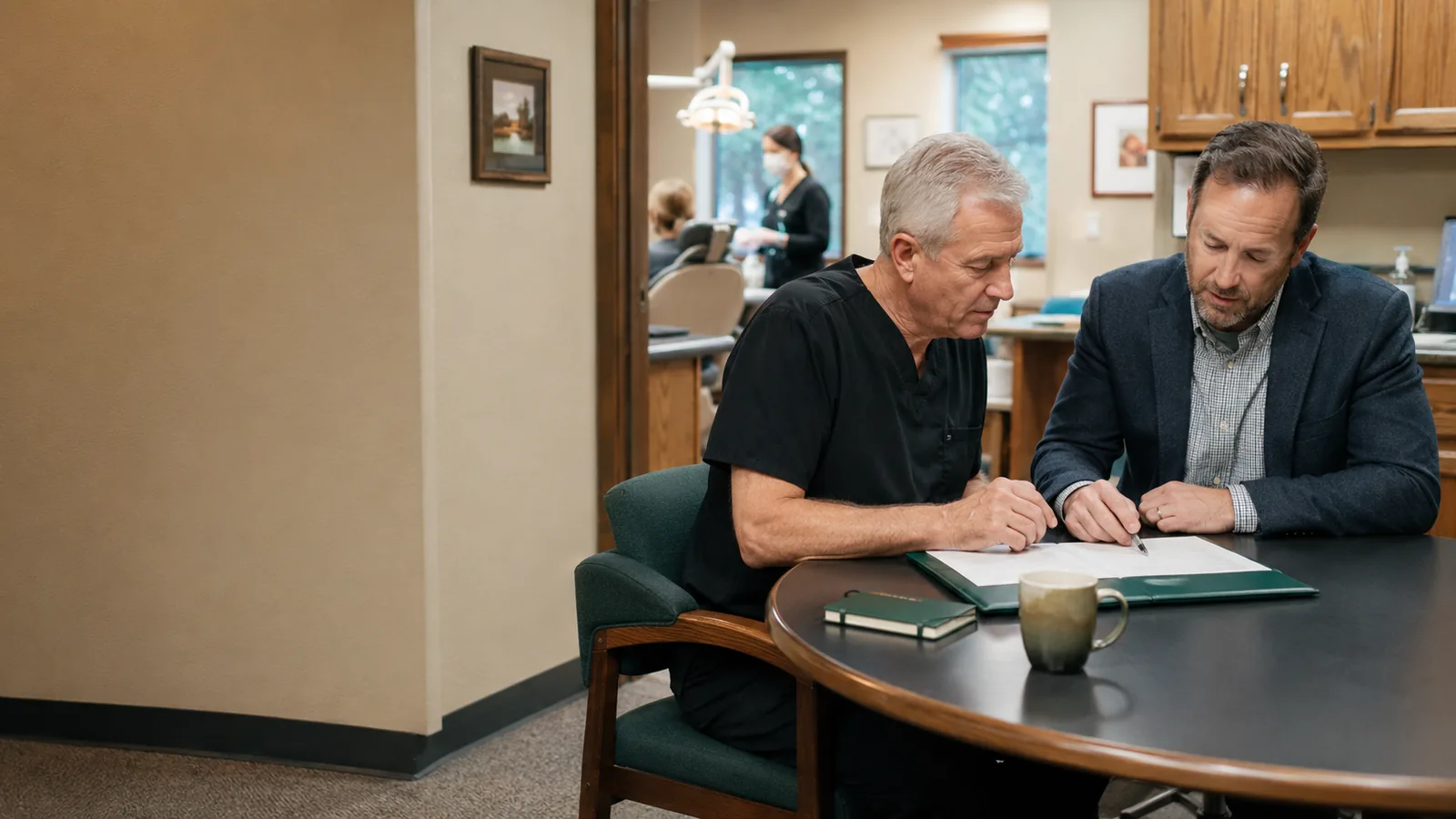 A dentist and an advisor signing partnership documents at a table.